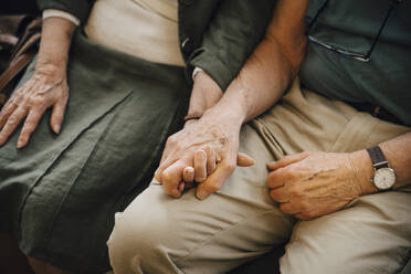 Midsection of senior couple holding hands sitting at nursing home - MASF16202