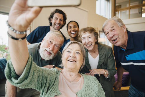 Senior woman taking selfie with friends and healthcare workers at retirement home - MASF16205