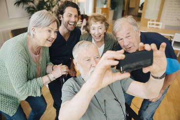 Disabled senior man taking selfie with friends and male nurse at retirement home - MASF16208