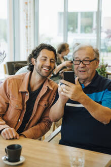 Ein älterer Mann macht ein Selfie mit seinem Enkel, während er am Esstisch eines Altenheims sitzt - MASF16223