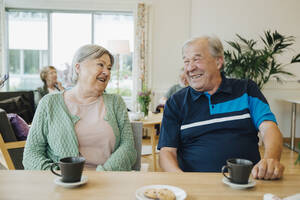 Lächelnde ältere Freunde, die sich am Esstisch eines Pflegeheims unterhalten - MASF16249
