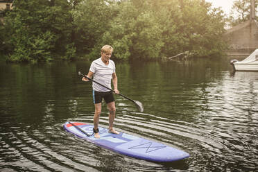 Full length of senior man paddleboarding in sea during SUP course - MASF16286