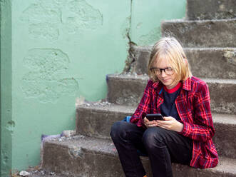 Tween lächelnd auf der Treppe sitzend mit Smartphone - CAVF72589