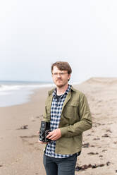 Porträt eines jungen Mannes mit Filmkamera am Strand - CAVF72592