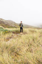 Junger Mann steht in einem Seegrasfeld an der Küste - CAVF72596