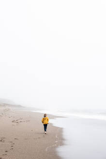 Teenager walks along oceans edge on quiet beach - CAVF72597