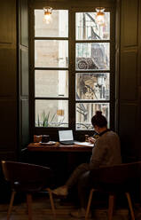 Junge Studentin studiert in einem Café mit ihrem Laptop - CAVF72611