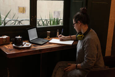 Junge Studentin studiert in einem Café mit ihrem Laptop - CAVF72612