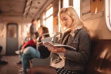 Young woman reading magazine while traveling in subway train - CAVF72614
