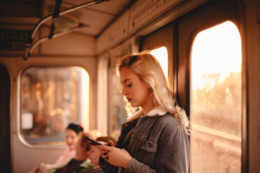 Young woman using smart phone while traveling in subway train - CAVF72618