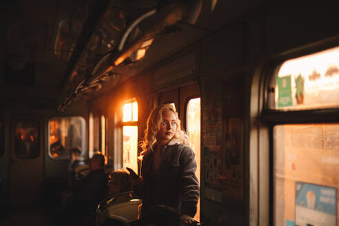 Young woman looking through window traveling in subway train - CAVF72621