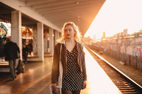 Junge Frau wartet auf einen Zug in einer U-Bahn-Station bei Sonnenuntergang, lizenzfreies Stockfoto