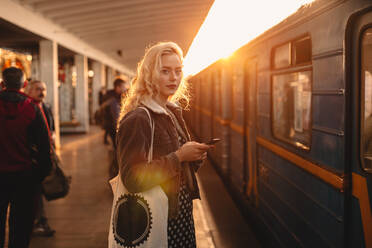 Junge Frau mit Smartphone an einer U-Bahn-Station - CAVF72629