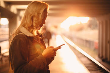 Junge Frau mit Smartphone beim Warten auf den Zug in der U-Bahn-Station - CAVF72631