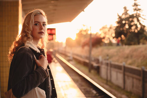 Young woman waiting for train at subway station during sunset - CAVF72633