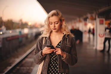 Junge Frau mit Smartphone beim Warten auf den Zug in der U-Bahn-Station - CAVF72640