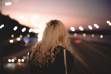 Rückansicht einer jungen Frau, die auf einer Brücke in der Stadt steht und auf die Straße schaut - CAVF72646