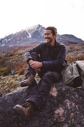 Glücklicher Wanderer sitzt auf einem Stein in den Bergen - CAVF72663