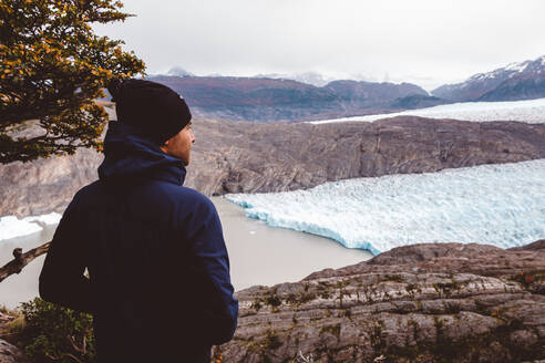 Mann steht und genießt den Blick auf See und Gletscher - CAVF72694