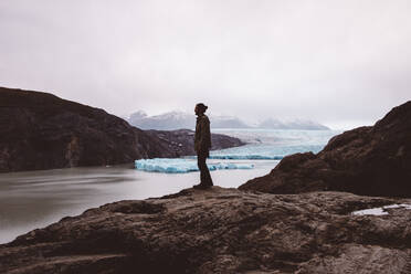 Mann steht auf einem Felsen am See mit Gletschern - CAVF72696