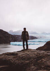 Man standing smiling on rock by lake with glaciers - CAVF72700