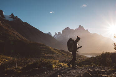 Rucksacktourist, der in den Bergen bei strahlendem Sonnenschein auf sein Mobiltelefon schaut - CAVF72706
