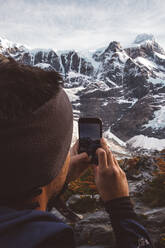 Crop traveler shooting snowy mountains with smartphone - CAVF72715