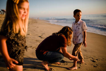 Mutter fesselt die Hose des Sohnes am Strand, während die Schwester wartet - CAVF72738
