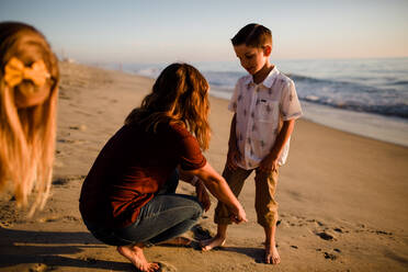 Mom Cuffs Son's Pants on Beach at Sunset While Sister Waits - CAVF72739