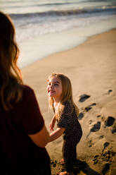 Tochter lächelt Mama am Strand bei Sonnenuntergang an - CAVF72742