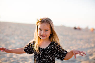 Young Girl Playing on Beach, Smiling at Camera at Sunset - CAVF72746
