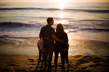 Vierköpfige Familie am Strand stehend, Blick auf den Ozean bei Sonnenuntergang - CAVF72749