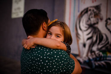 Father Hugging Daughter as Daughter Peers Over Shoulder - CAVF72764