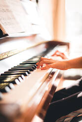 Ausgeschnittenes Bild von Kinderhänden, die in einem sonnigen Raum Klavier spielen. - CAVF72813