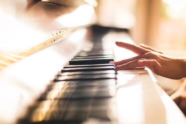 Nahaufnahme einer Kinderhand beim Klavierspielen in einem sonnigen Raum. - CAVF72815