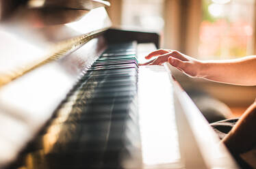 Ausgeschnittenes Bild einer Kinderhand, die in einem sonnigen Raum Klavier spielt. - CAVF72816