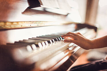 Cropped image of child's hand playing piano in a sunny room. - CAVF72817