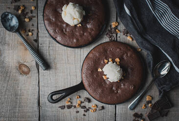 Draufsicht auf Brownies mit Eis und Nüssen in gusseisernen Bratpfannen. - CAVF72826