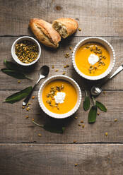 Draufsicht auf Schalen mit Butternusskürbissuppe auf einem rustikalen Holztisch. - CAVF72833