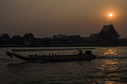 Ein Longtailboot fährt bei Sonnenuntergang auf dem Chao Phraya River, Bangkok, Thailand. - CAVF72841