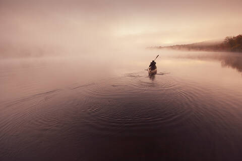 Solo-Paddeln auf einem nebligen Teich bei Sonnenaufgang., lizenzfreies Stockfoto