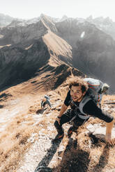 Young hiker climbing a steep mountain path in front of mountains - CAVF72886