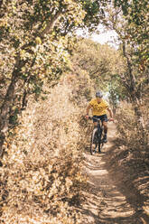 Junger Mann fährt Mountainbike auf staubigem Singletrail - CAVF72887