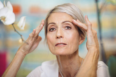 Porträt einer 67-jährigen Frau, die ihre Hände in der Nähe der Augenbrauen hält - CAVF72909