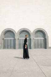 Young woman in long black dress posing in front of the building doors - CAVF72913
