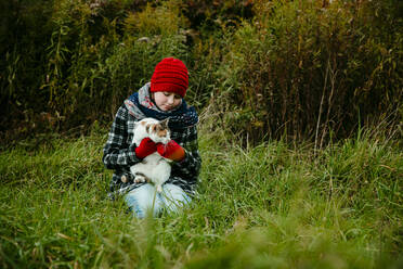 Junges Mädchen hält ihre Katze an einem kalten Oktobertag im Freien - CAVF72918