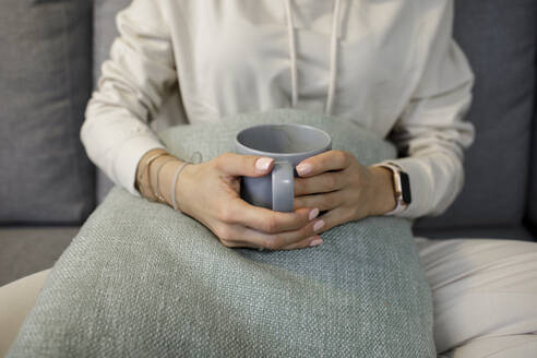 Crop-Ansicht von Frau entspannt mit Tasse Tee auf der Couch zu Hause - KMKF01180