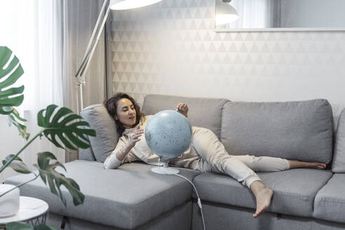 Porträt einer Frau, die zu Hause auf der Couch liegt und den Globus betrachtet - KMKF01185