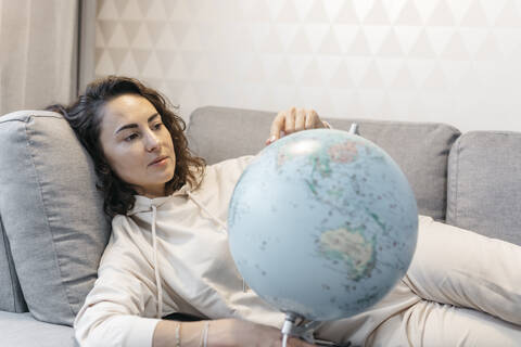 Porträt einer Frau, die zu Hause auf der Couch liegt und den Globus betrachtet, lizenzfreies Stockfoto