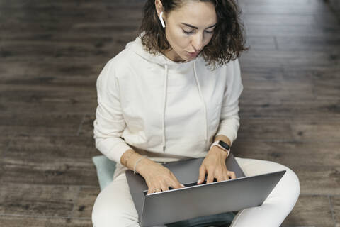 Frau sitzt zu Hause auf dem Boden und benutzt Laptop und Kopfhörer, lizenzfreies Stockfoto